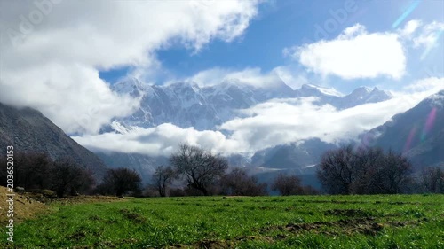 Snowy Mountain Peaks Above Green Meadow and Clouds