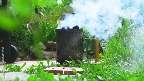 Charcoal briquettes glowing in a metal chimney starter, sending blue smoke skyward as the grill heats up for backyard bbqs, summer cookouts and weekend gatherings