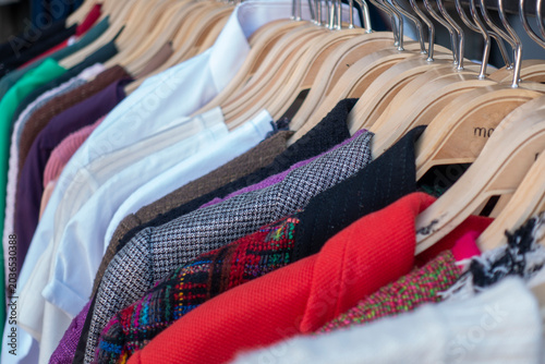 Different women's clothes hanging on rack against yellow background. Space for text