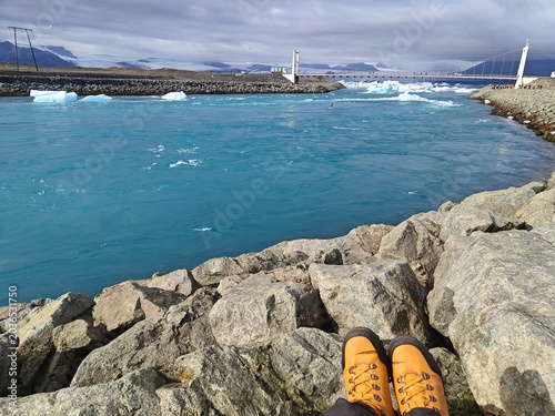 POV of traveler in yellow hiking boots looking at floating icebergs in Jökulsárlón glacial lagoon, Iceland. Adventure, freedom and Nordic nature exploration concept.