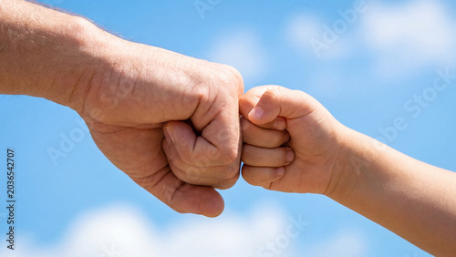 A powerful father and child fist bump against a bright blue sky, symbolizing support, connection, and teamwork