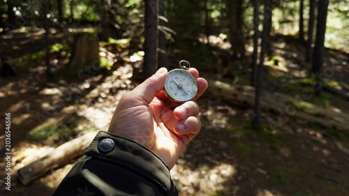 A hand holds a compass against the backdrop of lush trees. Sunlight filters through the branches, creating a peaceful atmosphere perfect for adventure and discovering new paths in nature