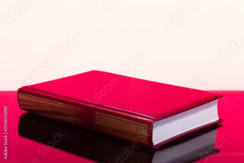 A closed red book on a red table on a white background with a copy space