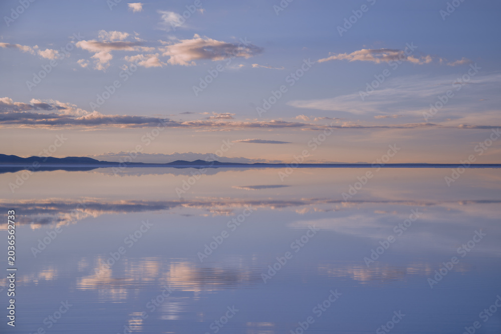 Fototapeta premium A breathtaking symmetrical reflection of sunset clouds on the flooded Salar de Uyuni salt flats in Bolivia. Perfect for travel, wellness, and conceptual backgrounds with ample copy space.