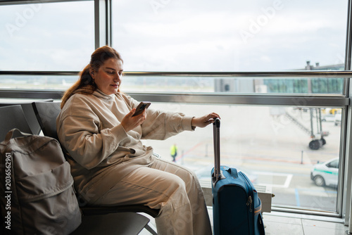 Young woman traveler sitting in airport waiting area and using smartphone. High quality FullHD footage