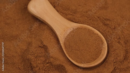 Cinnamon powder in wooden spoon close up, rotation. Warm, aromatic spice is a staple in baking and cooking