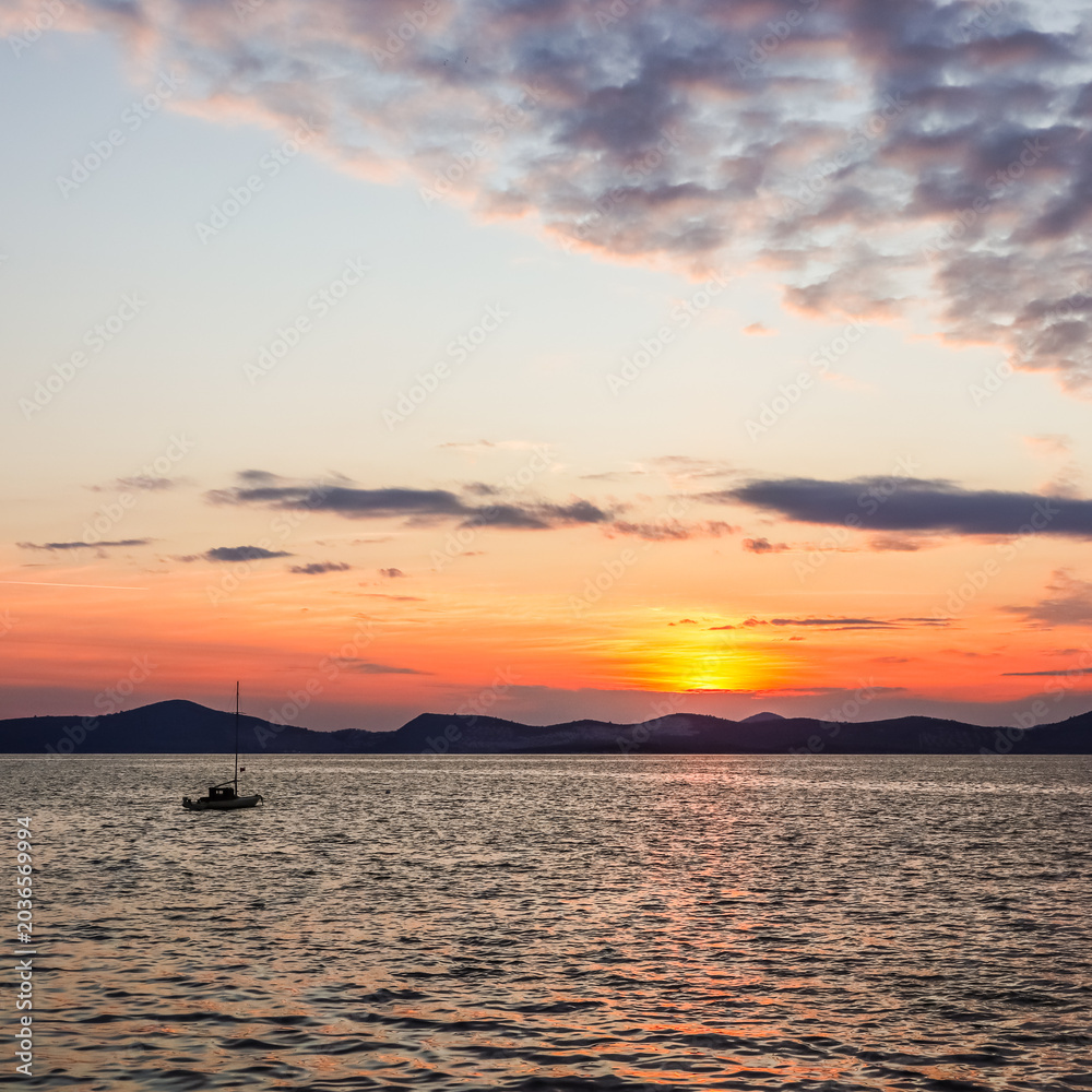 Obraz premium Calm evening sunset with a sailboat on the water, reflecting vibrant colors across the sky in Gulluk, Turkey