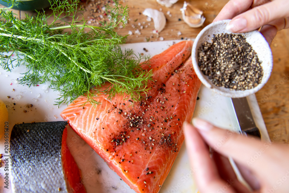 Fototapeta premium Salmon fillet being seasoned with pepper, garnished with fresh dill.