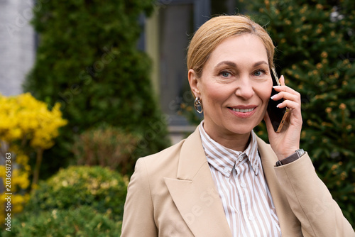 Φωτογραφία Elegant woman enjoying a sunny day while talking on the phone in a beautiful gar