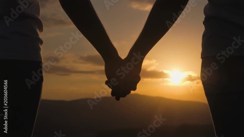 Silhouette of Couple Holding Hands Against a Golden Sunset Over Scenic Mountains
