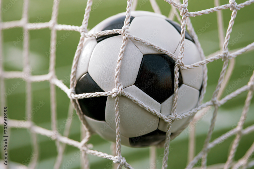 Naklejka premium Soccer ball nestled in net during a competitive match on a sunny day