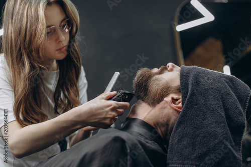 Schilderij op canvas Professional female barber trimming beard of male client with electric clipper d
