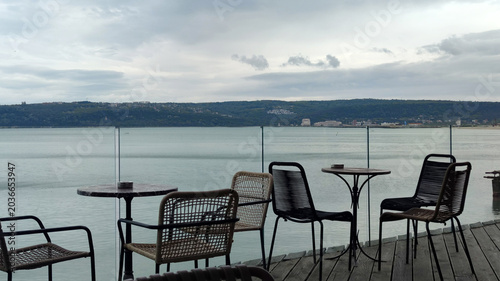 Quadro em tela outdoor cafe tables and chairs by sea under cloudy sky panoramic view
