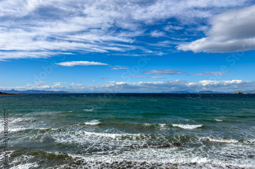 Картината върху платно Choppy waves roll toward the shore under scattered clouds and blue sky near Voul