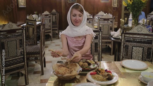 Slow motion shot of female traveler taking traditional bread at authentic restaurant in Cairo, Egypt. Woman in headscarf enjoying local Middle Eastern cuisine in cozy oriental interior.