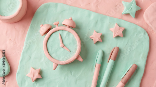 Clay style background featuring a pink alarm clock stars and pens on a textured surface