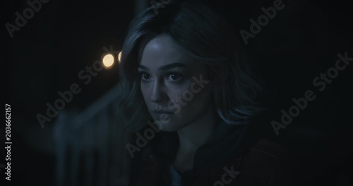 Glistening eyes of serious young woman looking around dark, scary home then down at notebook - tilt, closeup shot