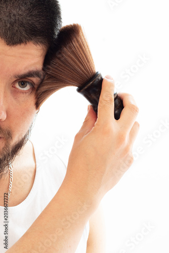 A man running a barber's brush over his temple to remove stray hairs after a haircut