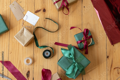 Large green gift sitting centered on light wooden table surrounded by ribbons, tags, tape