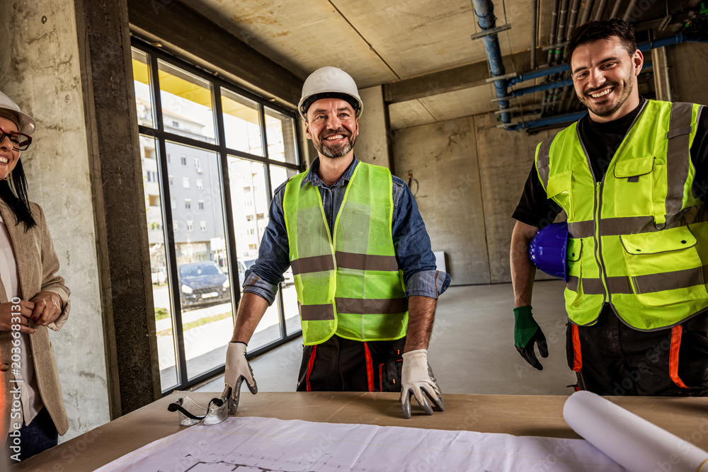 Obraz premium Construction crew and female architect talking around a table with blueprints.