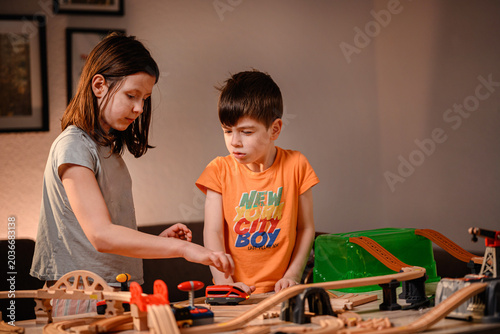 Brother and sister playing together with wooden toy train set on table in cozy evening room