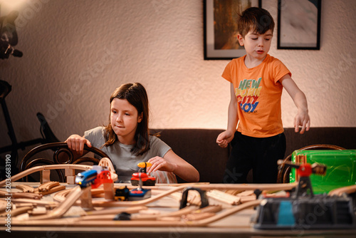 Active children playing with toy railway at home boy standing and girl focusing on wooden tracks
