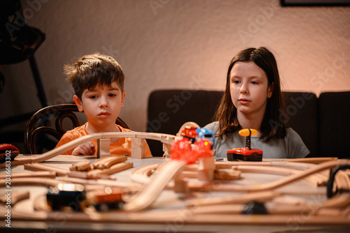 Brother and sister looking at wooden toy train set on table illuminated by warm evening light
