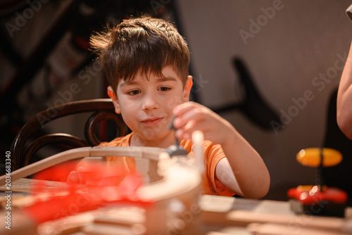 Concentrated young boy placing small detail on wooden toy railway track during indoor playtime