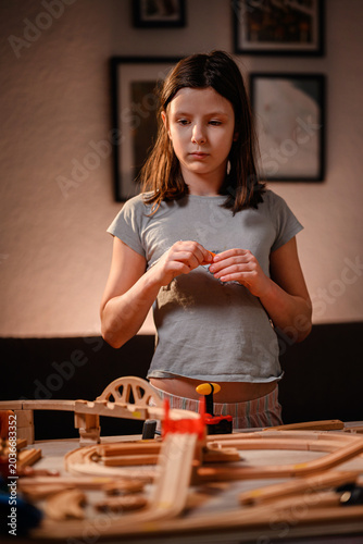 Thoughtful young girl holding wooden track piece building toy railway system in cozy room
