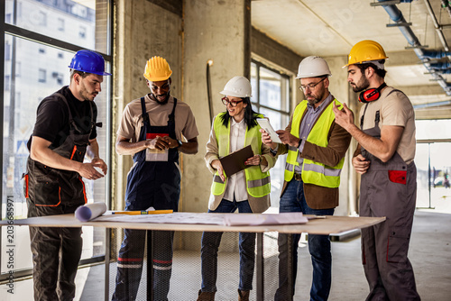 Construction workers and architects collaborating around a table with a digital tablet and building plans.