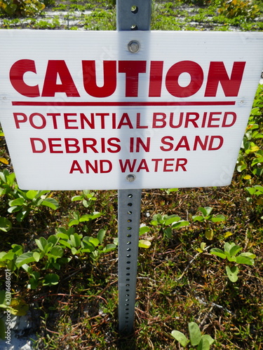 Caution potential buried debris in sand and water warning hazard sign in nature area vertical photo