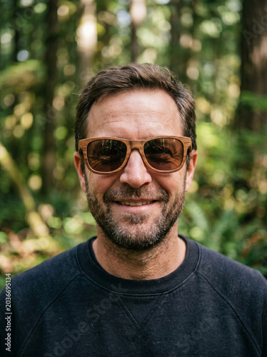 Happy mature man in sunglasses standing in a forest