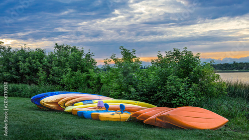 Canvastavla Plastic, kayak boats stored for the night, lined up on the grass sheltered by green shrubs