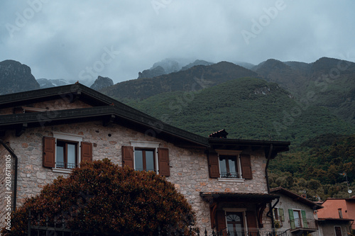 Stone village house with mountain backdrop and cloudy sky.