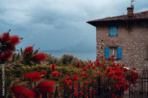 Stone house with blue shutters and red flowers overlooking Lake Garda.