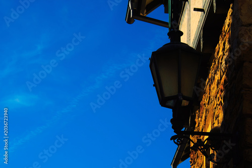 An old outdoor lantern in vintage style was hanging in the dark shadow of a wall.