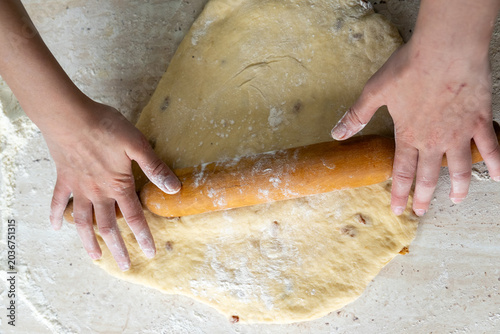 Tableau sur toile pair of hands uses a wooden rolling pin to flatten a piece of raw dough sprinkled with flour on a kitchen surface, preparing it for baking