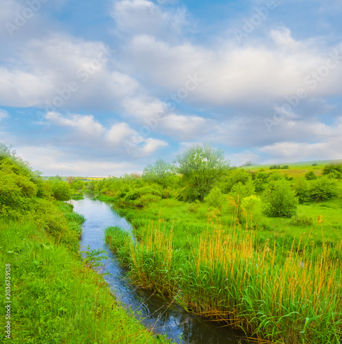 Canvas Print small river flow through green canyon under a blue cloudy sky