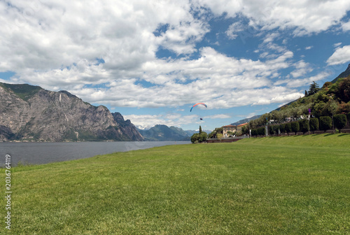 Paraglider over Lake Garda with grassy foreground and dramatic cloudscape.