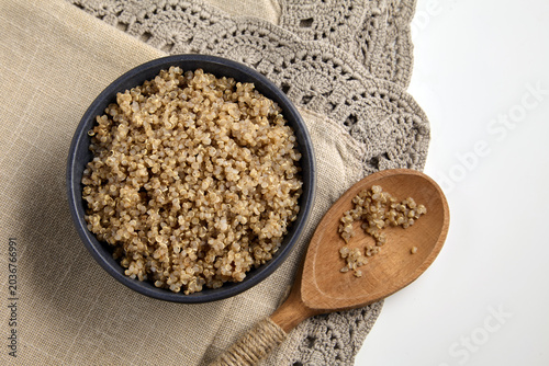 Foto Boiled buckwheat groats in a ceramic bowl and a wooden spoon on a linen tableclo