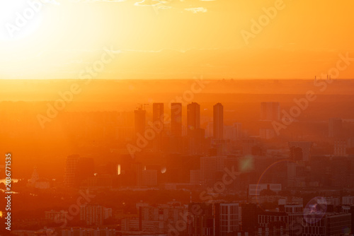 A breathtaking aerial view of the modern city skyline during a golden sunset. The cityscape, with skyscrapers and residential buildings, is bathed in the warm rays of the evening sun.