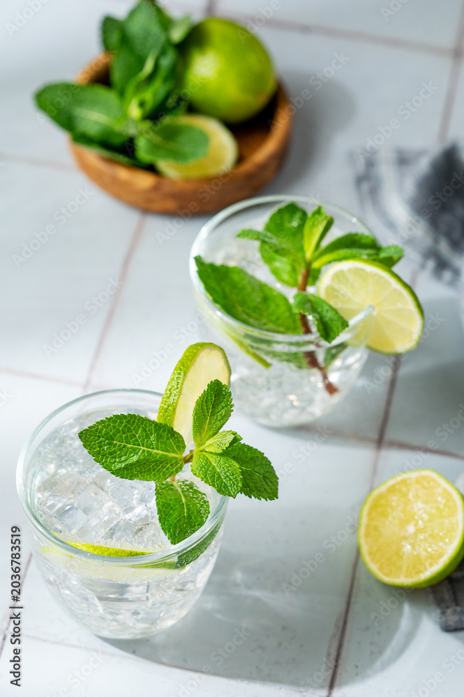 Fototapeta premium A fresh mojito with lime, mint and ice in glasses. Citrus lemonade or cocktail on a tile background