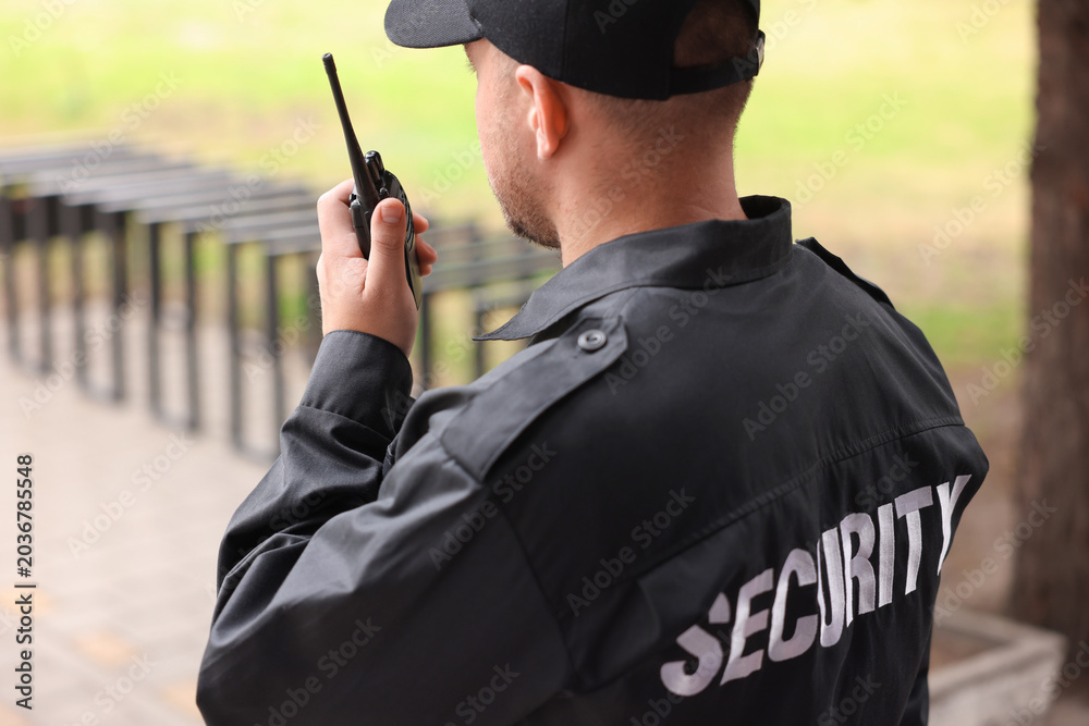 Obraz premium Security guard in uniform using walkie talkie outdoors