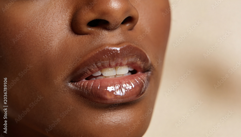 Fototapeta premium Woman with glossy lips in close up shot. Beauty portrait of African American female showing skincare and cosmetics application. Professional makeup concept for fashion or beauty industry.