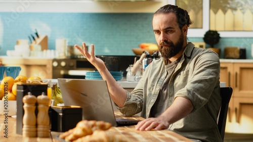 Bilde på lerret Uncertain person dealing with ambiguous remote job tasks at home, preoccupied with misunderstanding and disorganized data, Confused unsure man, frowning and struggling at kitchen table