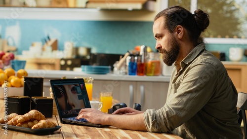 Tableau sur toile Professional graphic designer enhancing images on laptop in kitchen setting, Raw photos development with cinematic effects, color saturation and visual refinement, modern creative lifestyle