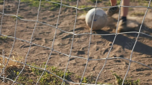 Slow motion close-up of football kick showing only legs striking ball on dusty street ground. Impact lifts dust into air. Street football training in urban or rural area, scoring action concept.