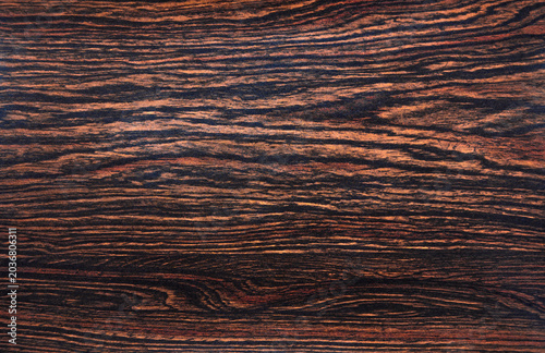 Photo of the background texture made of dark makassar wood.Dark wooden background for the text.The material for finishing luxury furniture.
