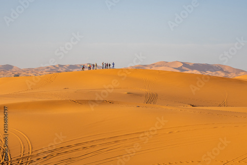 Tiny tourists standing on Sahara dune ridge in Merzouga desert, Morocco