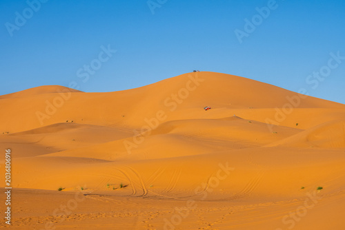 Off-road adventure vehicles and tourists exploring golden Sahara dunes near Merzouga, Morocco
